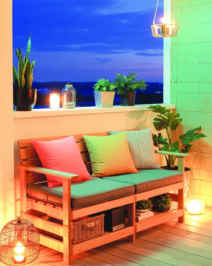 Foldable wooden bench with storage and cushions on cozy balcony at dusk.