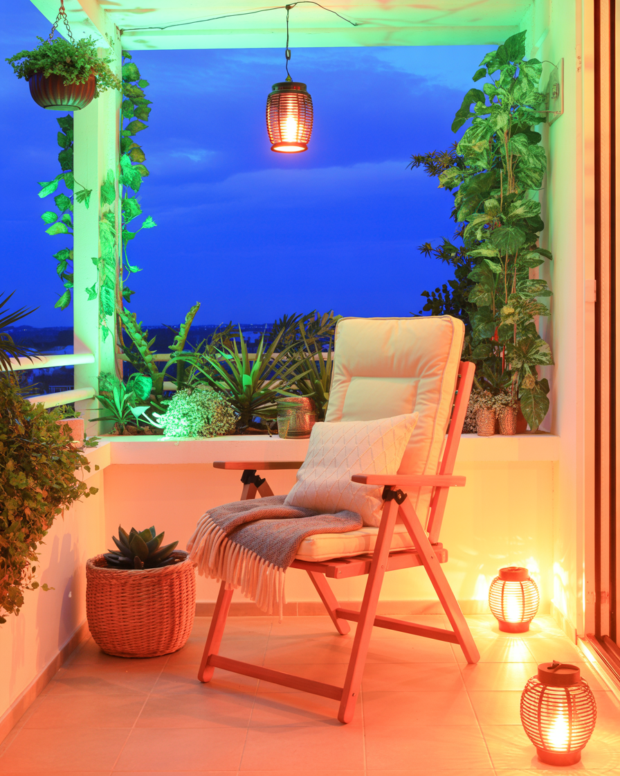Foldable reclining chair with cushions and plants on balcony during sunset.